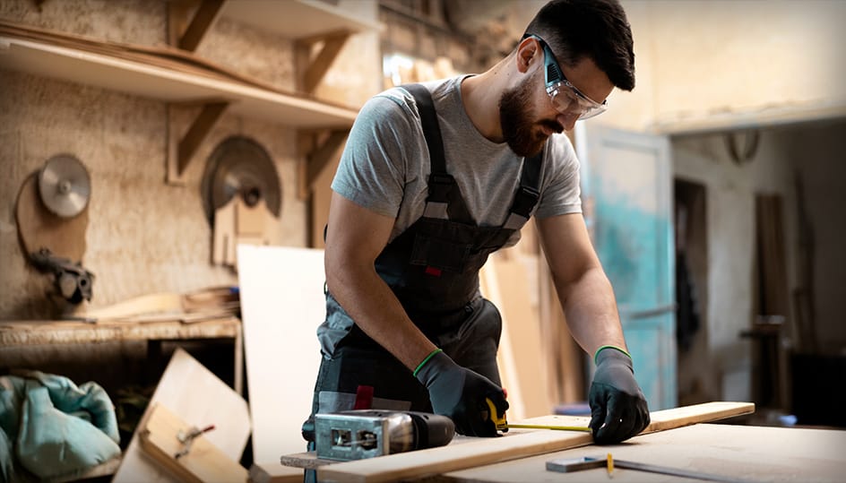 Timmerman meet nauwkeurig een houten plank in werkplaats. Precisie en vakmanschap bij houtbewerking door FB Bouwdiensten.
