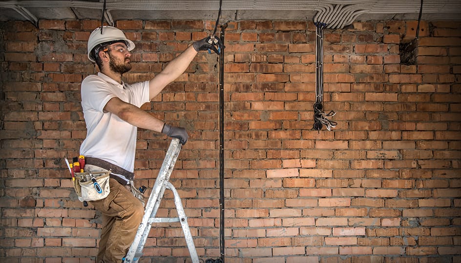Vakman op ladder voert elektrische werkzaamheden uit tijdens renovatie, vakkundige uitvoering door FB Bouwdiensten.